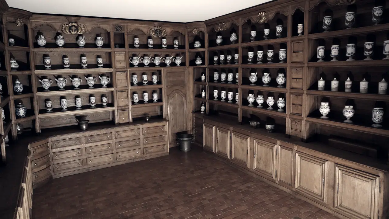 Ancienne apothicairerie reconstituée : boiseries à tiroirs et à placards, et étagères chargées de pots de pharmacie en faïence alignés par rangées.