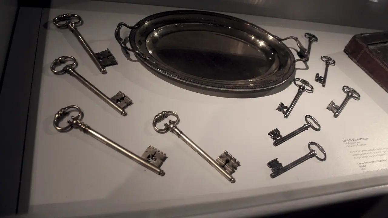 Douzaine de grandes clés anciennes disposées autour d'un plateau ovale dans une vitrine de musée, avec le cartel imprimé posé à côté.