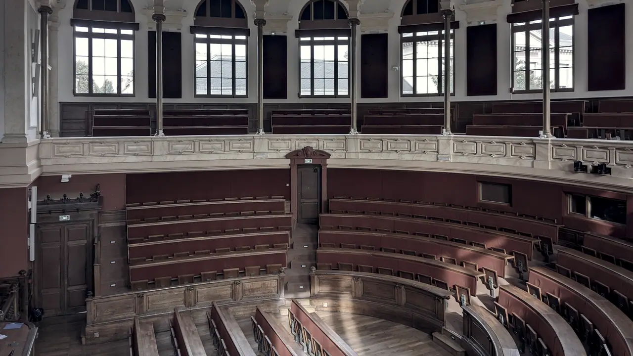 Grand amphithéâtre vide, avec ses gradins de bois disposés en arc de cercle sous une galerie de hautes fenêtres, et sa chaire étroite.