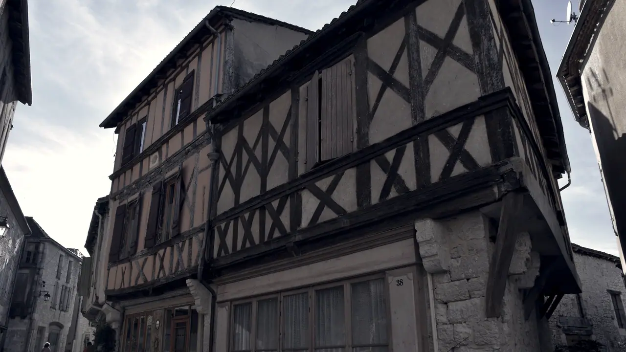 Maison à colombages en encorbellement : l'étage avance au-dessus de la rue, plus large que le rez-de-chaussée qui le porte, appuyé sur un pilier de pierre.