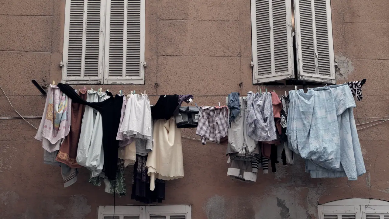 Linge qui sèche sur un fil tendu sous deux fenêtres aux volets clos, devant une façade à l'enduit défraîchi où s'ouvrent deux autres fenêtres plus bas.