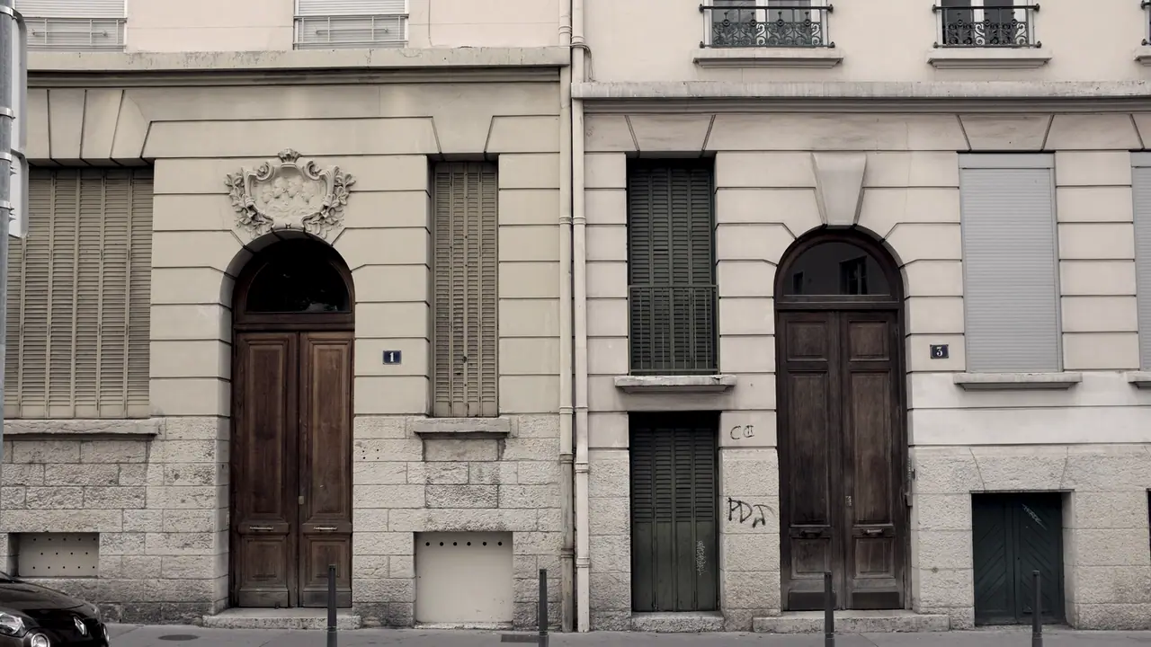 Deux portes d'immeuble en bois à encadrement cintré alignées sur une même rue, avec un cartouche sculpté au-dessus de l'une et un soubassement en pierre.