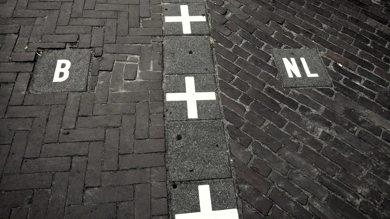 Ligne de dalles marquées de croix qui partage un trottoir pavé en deux, avec la lettre B d'un côté et les lettres NL de l'autre, à la frontière de Baarle.