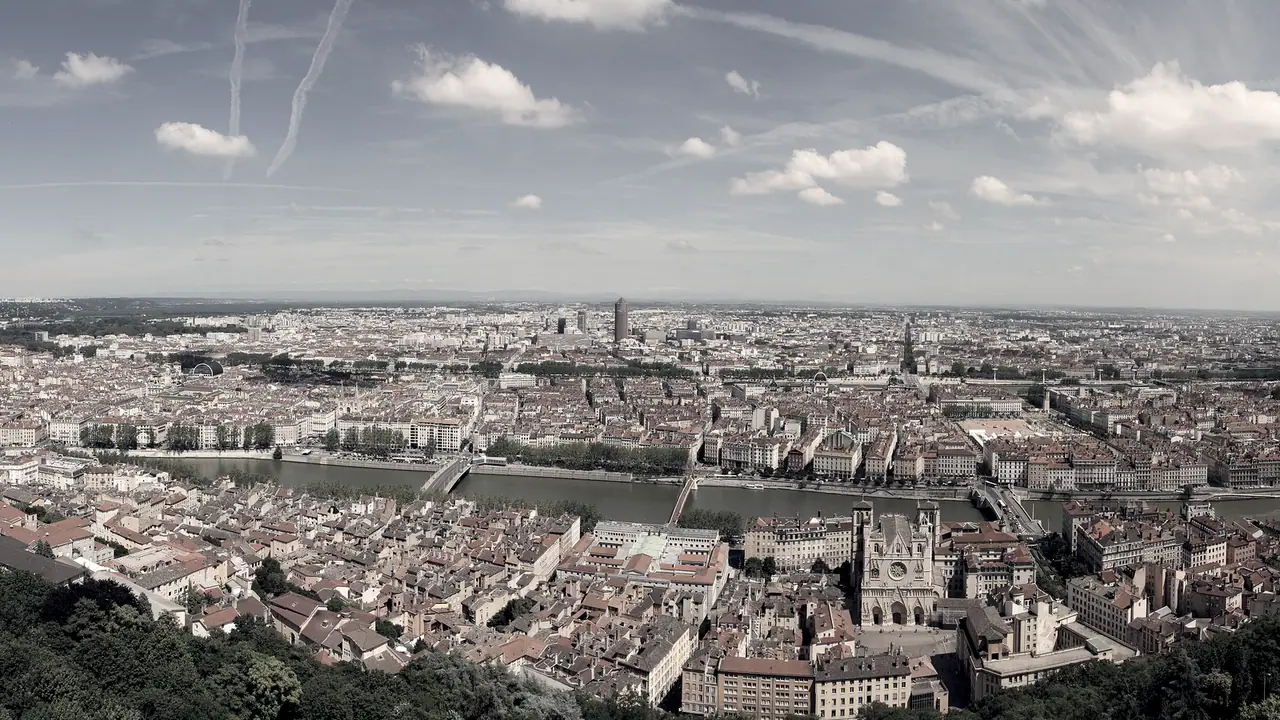 Vue aérienne de Lyon : les toits de tuiles s'étendent sur tout l'horizon, traversés par le fleuve et coupés par les grands axes.