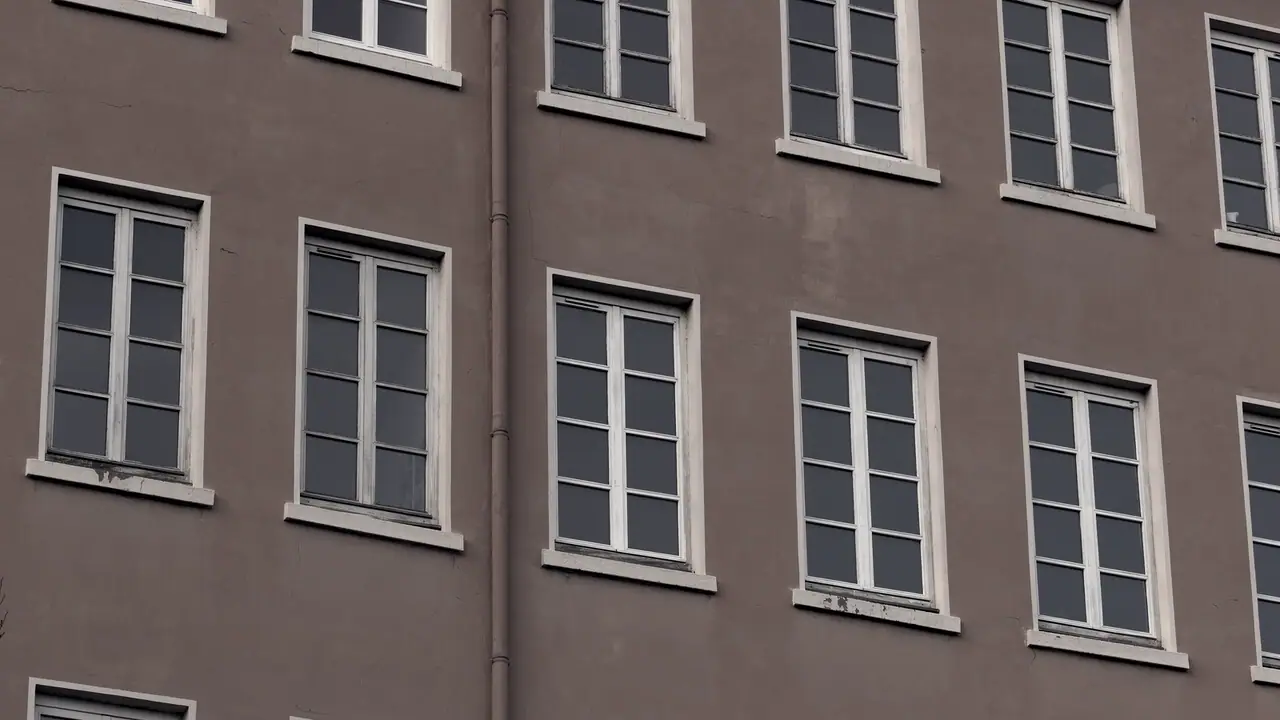 Façade crépie d'un immeuble de canuts, percée de rangées régulières de hautes fenêtres à petits carreaux, sur plusieurs étages.