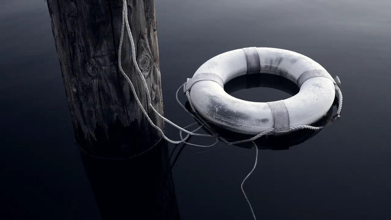 Bouée de sauvetage couverte de givre qui flotte sur un lac immobile, reliée par une corde à un pieu de bois planté dans l'eau.