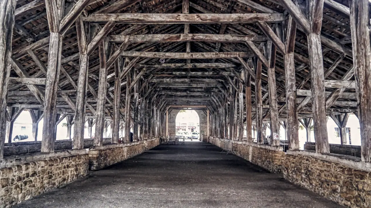 Intérieur d'une halle ancienne à Crémieu : une seule charpente de bois portée par deux rangées de poteaux, posés sur des murets de pierre, jusqu'au jour du fond.