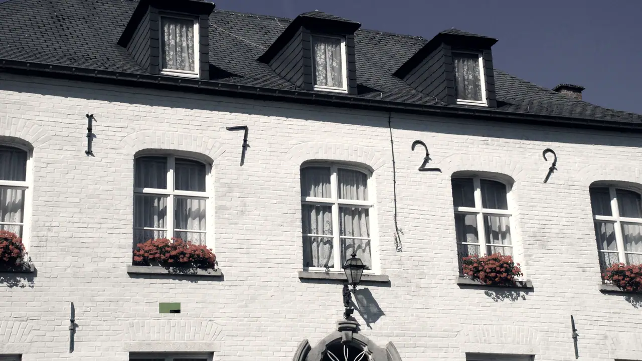 Façade de brique peinte d'une maison ancienne dont les ancres de fer dessinent la date « 1729 », sous trois lucarnes d'ardoise, avec des fenêtres fleuries et une lanterne.