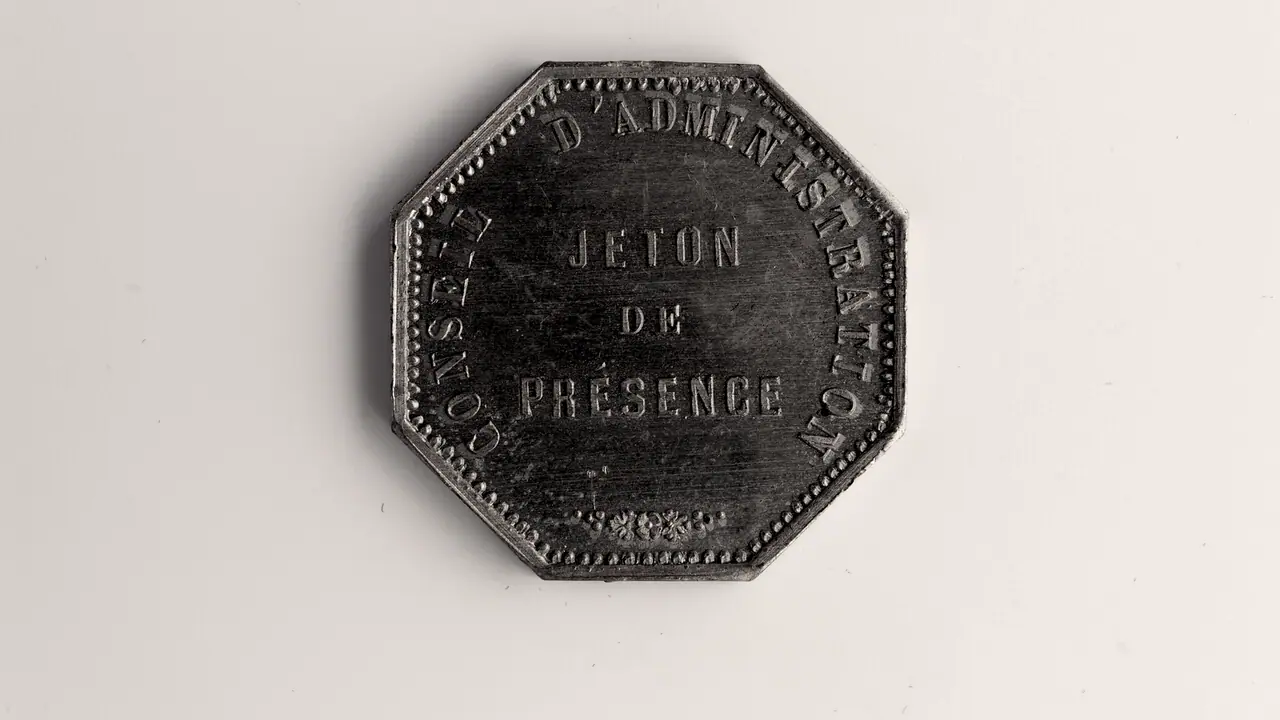Jeton octogonal en métal gravé « jeton de présence », posé à plat, ses lettres en relief usées par le frottement.