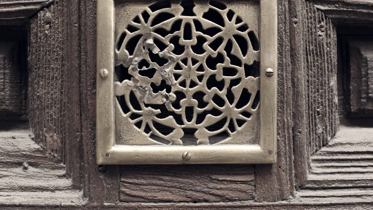 Judas carré en laiton ajouré, vissé au centre d'une porte ancienne en bois sculpté, son entrelacs d'étoiles masquant l'ouverture.