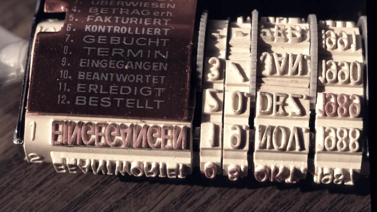 Tampon dateur de bureau à molettes de caoutchouc, avec son sélecteur de mentions en allemand, dont « contrôlé » et « reçu », et ses rouleaux de jours, de mois et d'années.