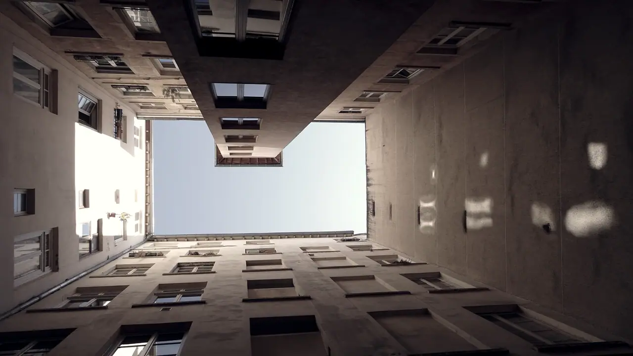 Cour intérieure étroite vue depuis le sol : des façades anciennes percées de fenêtres montent de tous côtés vers un rectangle de ciel.