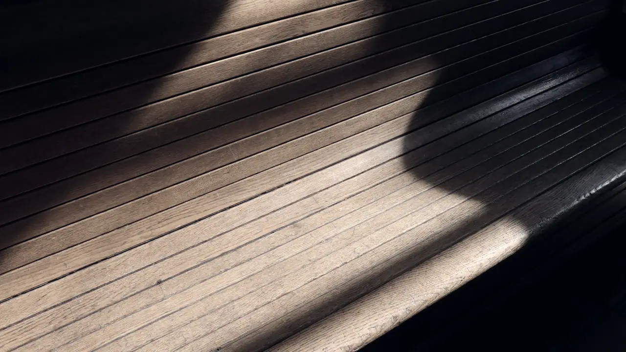 Banc à lattes de bois d'une ancienne salle d'attente de gare, traversé par une bande de soleil oblique dans la pénombre.