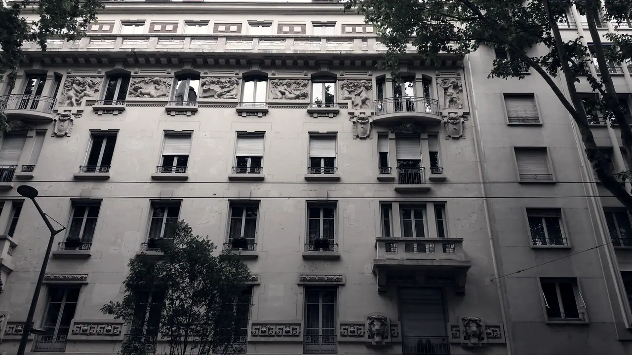 Façade d'immeuble bourgeois avec des frises sculptées sous la corniche et des balcons en fer forgé devant chaque fenêtre.