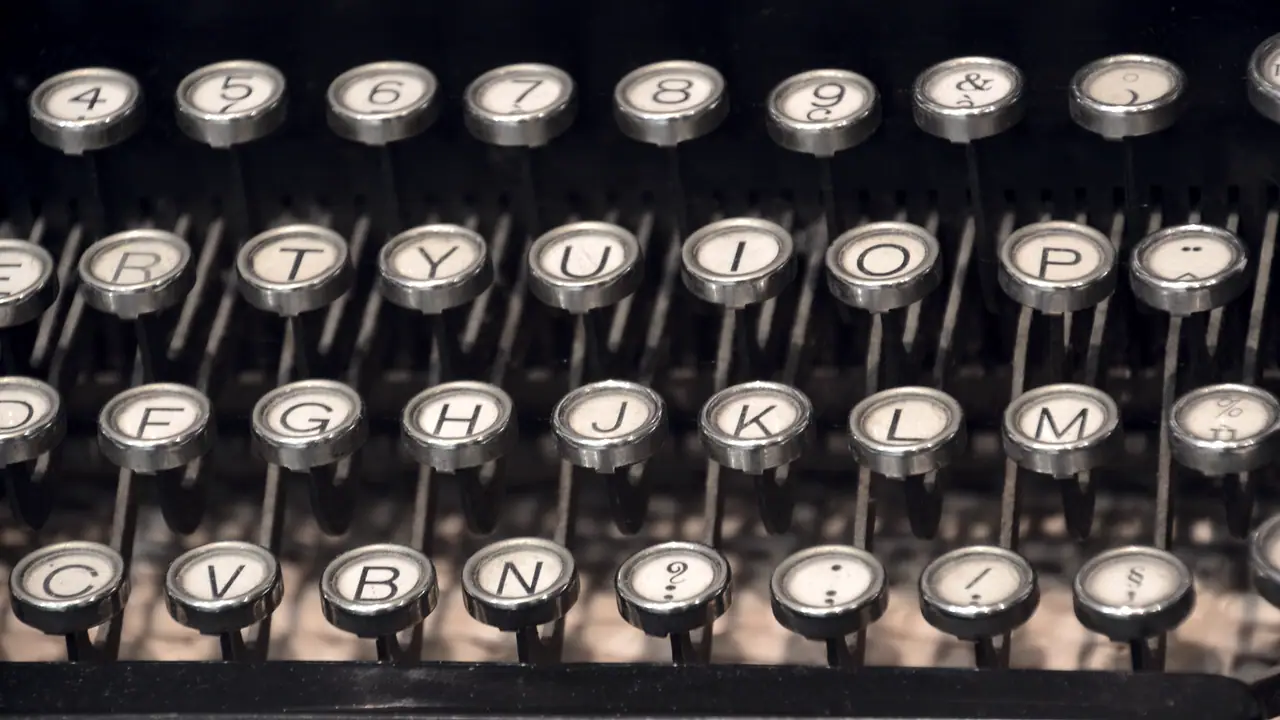 Touches rondes cerclées de métal d'une machine à écrire ancienne, en rangées décalées de lettres et de chiffres, avec le point d'interrogation sur la rangée du bas.