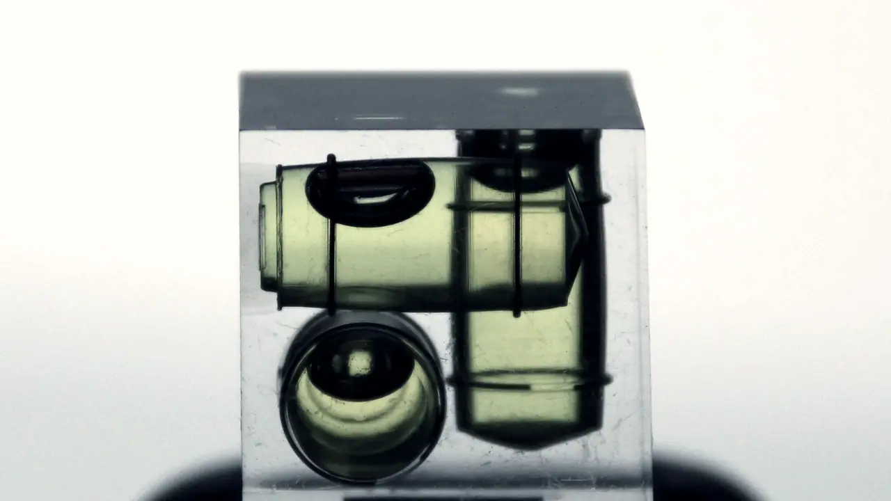 Niveau à bulle cubique en résine transparente, avec trois fioles vertes orientées dans des directions différentes, sur un fond clair.
