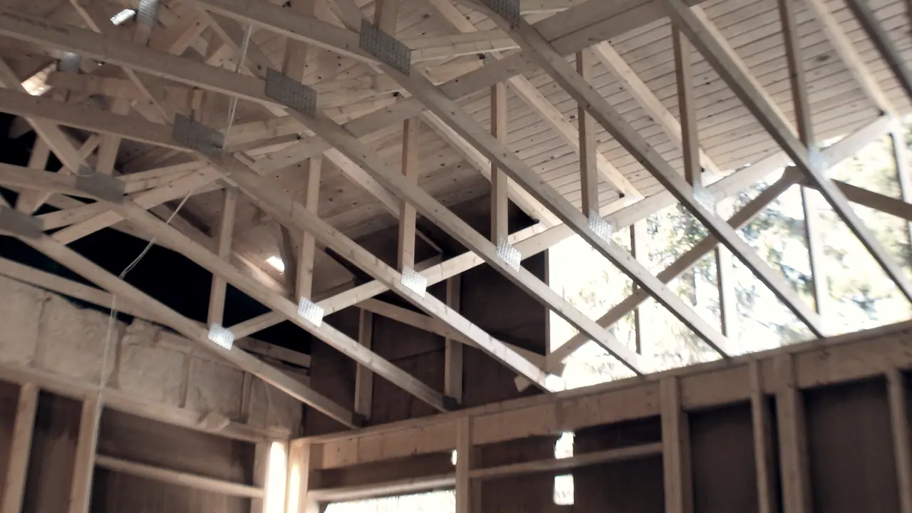 Charpente de bois vue de l'intérieur, avec ses fermes assemblées par des plaques métalliques et les murs encore nus sous elle.