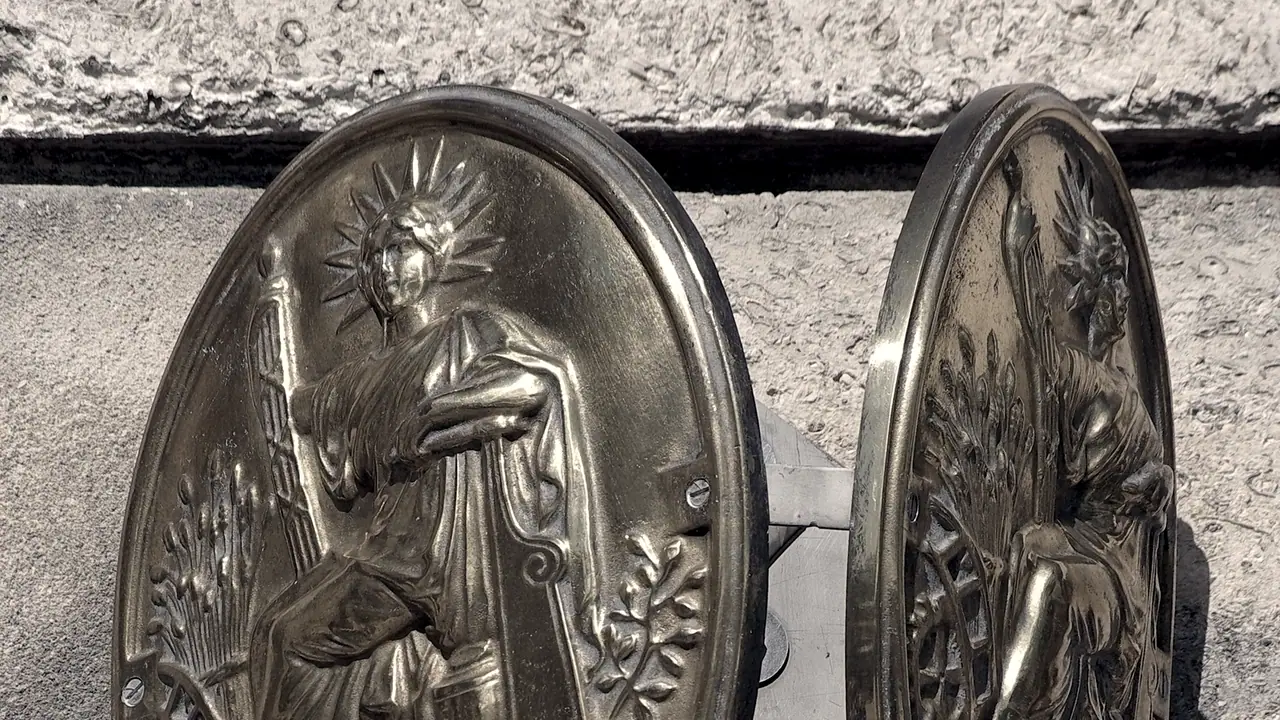 Deux panonceaux ovales de notaire en métal repoussé, fixés sur un mur de pierre, chacun orné d'une figure allégorique assise.