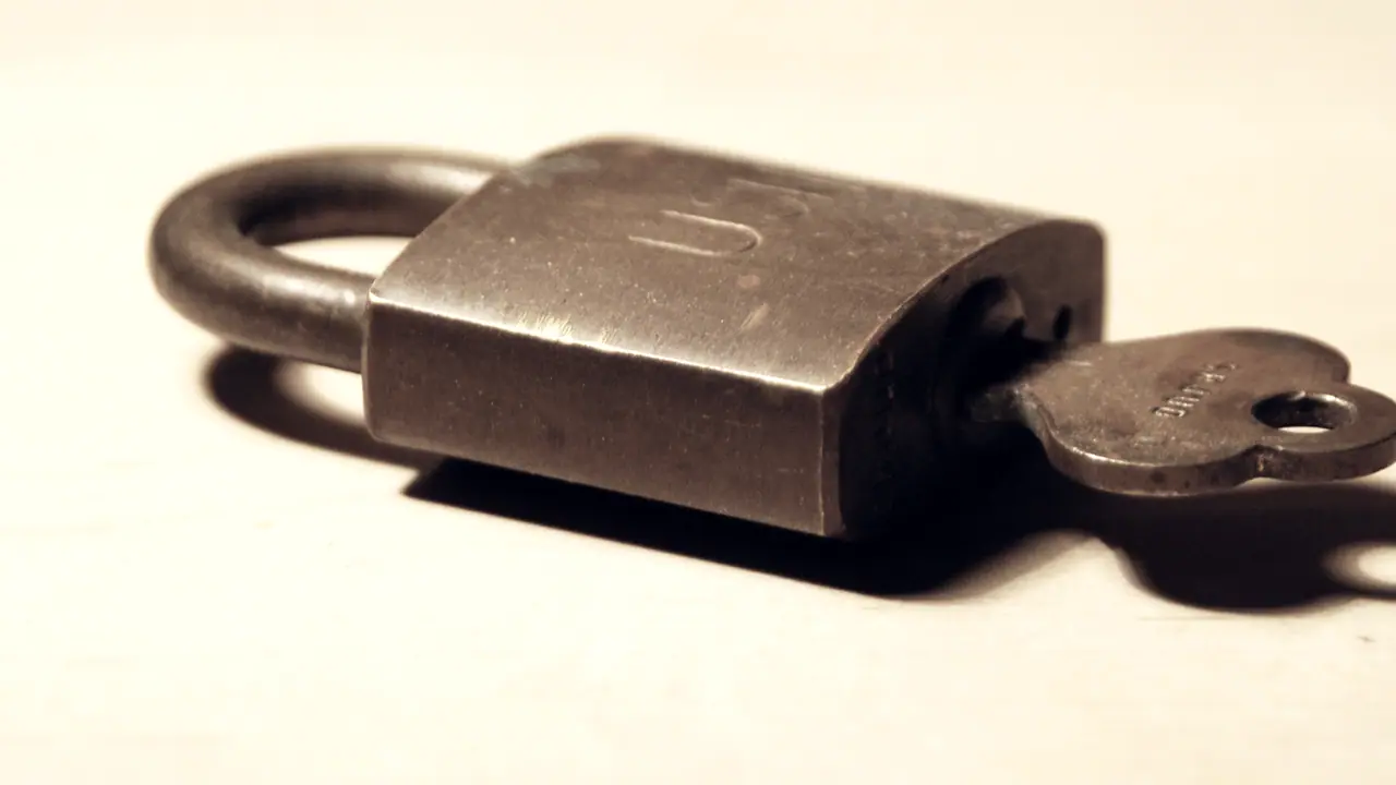 Cadenas fermé posé à plat sur un fond uni, avec son anse épaisse et sa clé engagée dans la serrure.