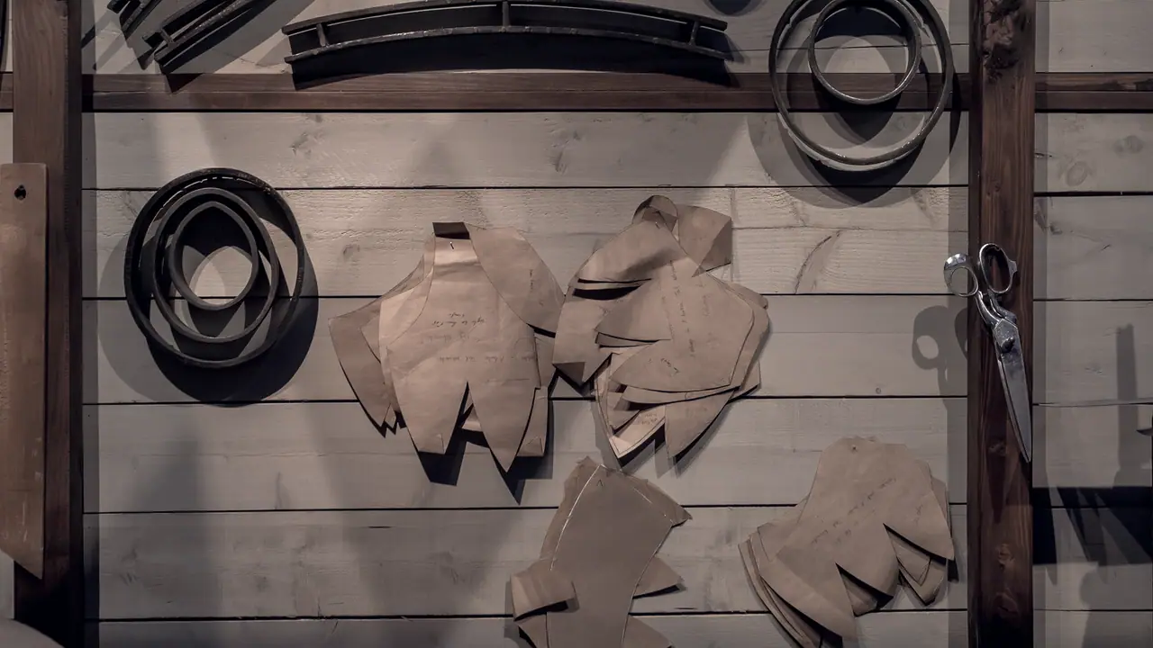 Patrons de coupe en papier kraft accrochés au mur de planches d'un atelier, entre des gabarits de métal cintrés et une paire de ciseaux.