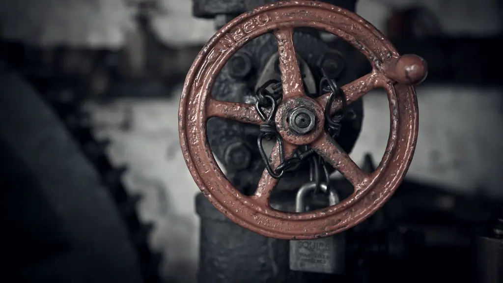 Volant de manœuvre à rayons d'une vanne industrielle, entravé par une chaîne et un cadenas, sur un corps de fonte sombre dans la pénombre d'un local technique.