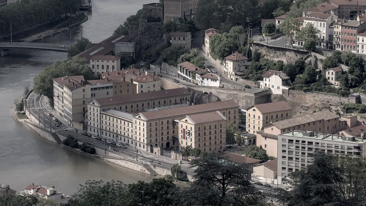 Depuis les hauteurs, un long bâtiment ancien aux nombreuses fenêtres s'étire entre un fleuve et un coteau bâti en terrasses.