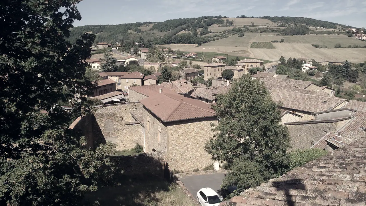 Toits de tuiles d'un village ancien serrés autour d'une église en pierre, avec des collines cultivées au fond.