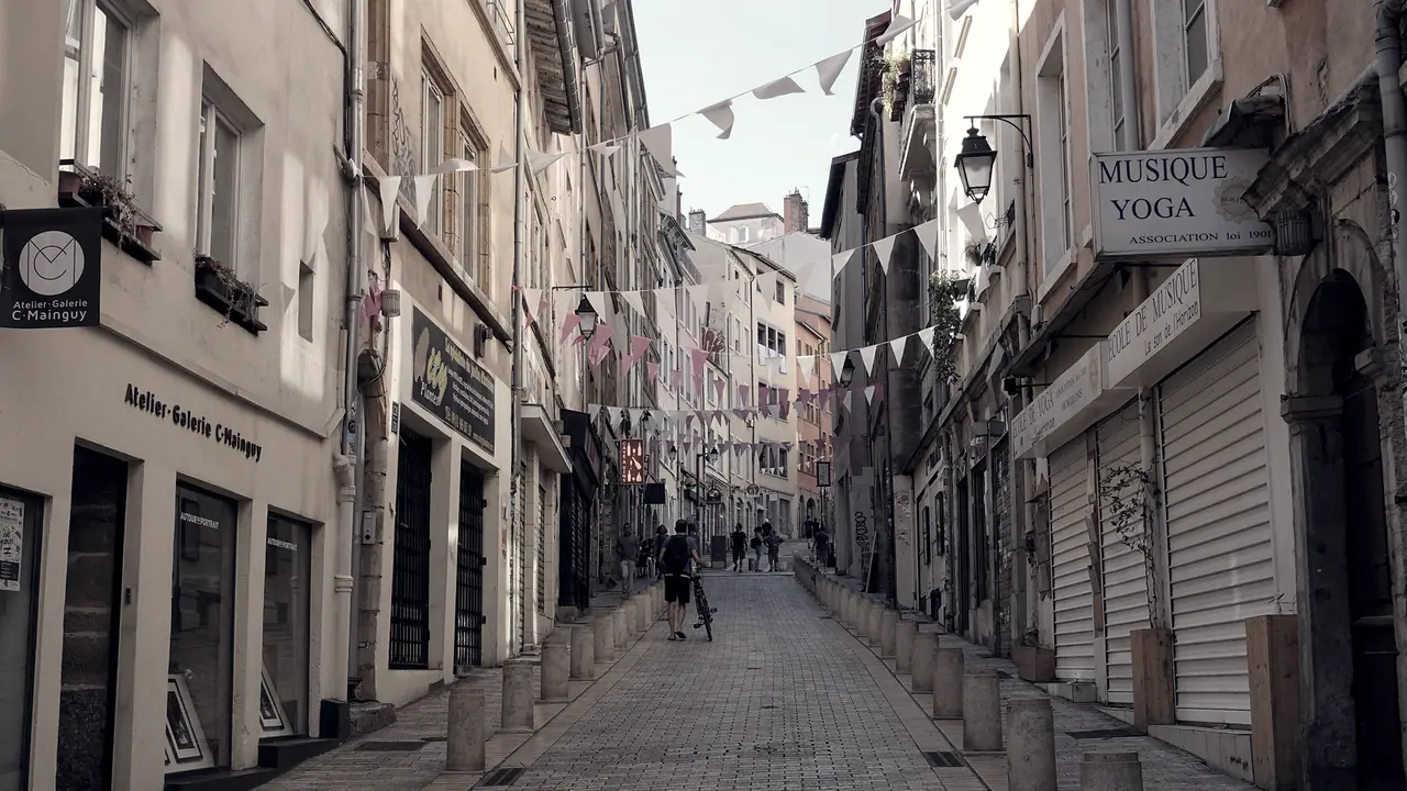 Rue pavée en pente bordée d'immeubles anciens, avec des fanions tendus entre les façades et quelques passants qui la remontent.
