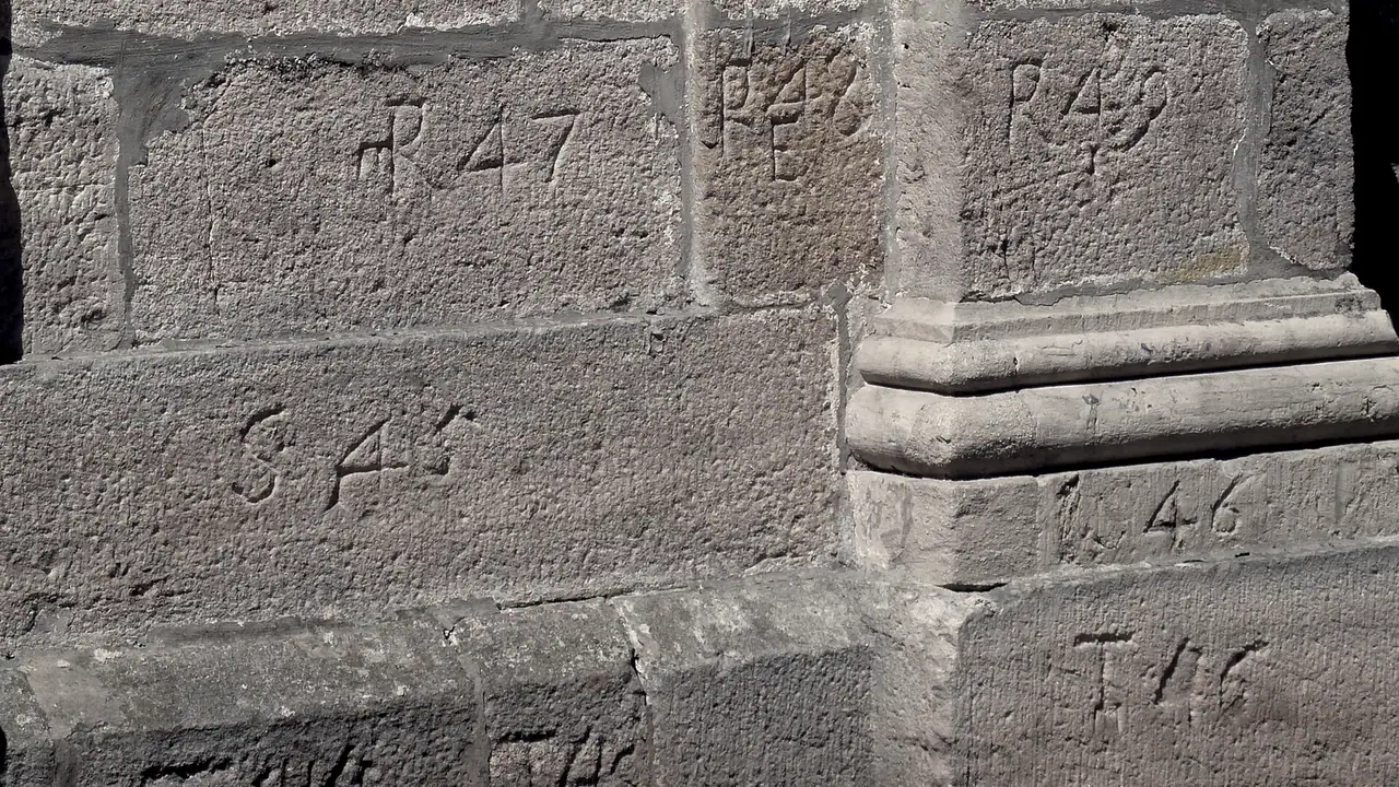 Pierres de taille d'un mur de chapelle, chacune gravée d'une lettre et d'un numéro qui fixent sa place dans l'appareil, au pied d'un pilier mouluré.
