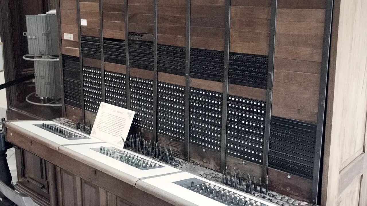 Ancien standard téléphonique manuel en bois exposé dans un musée : des panneaux percés de centaines de jacks au-dessus d'une tablette hérissée de fiches.