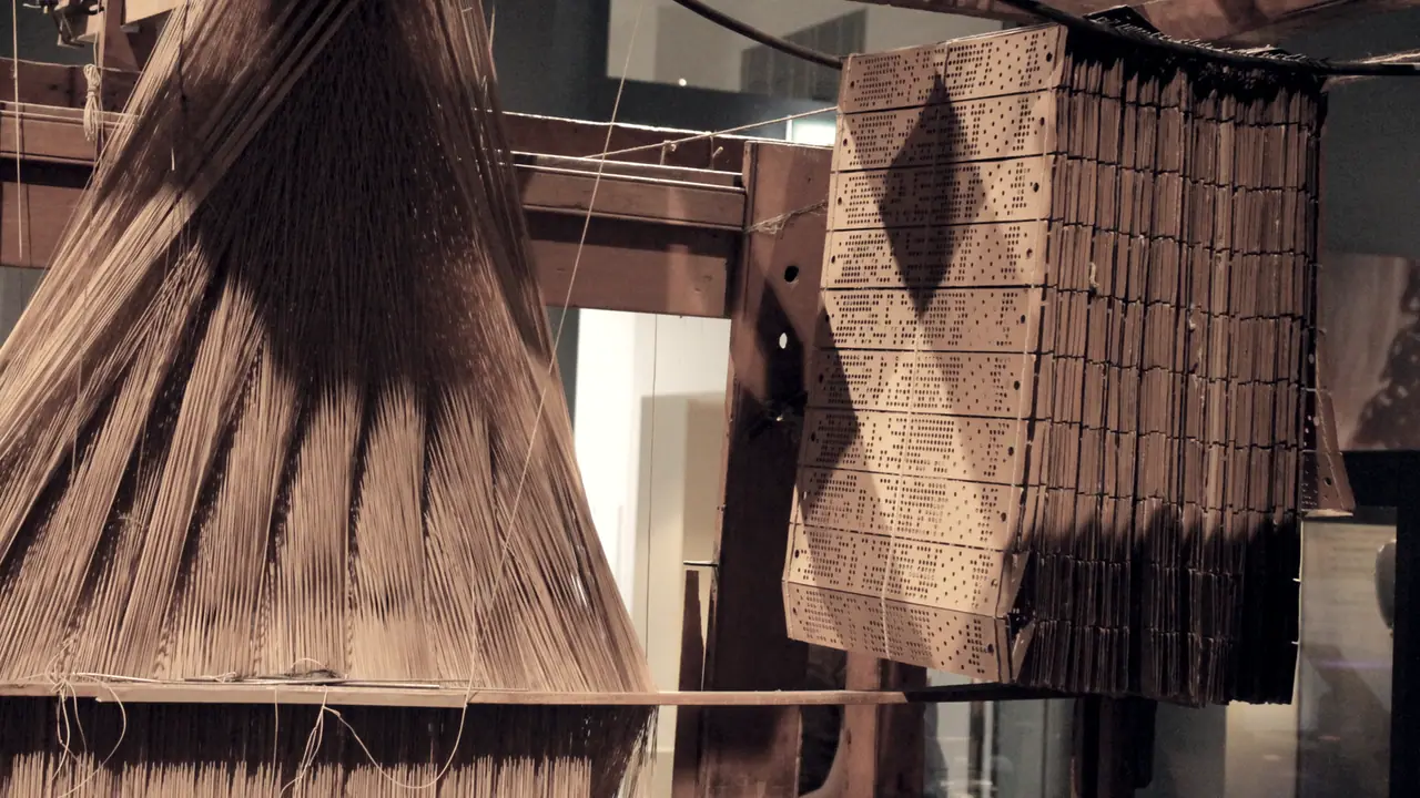 Métier Jacquard dans un musée : à droite, la chaîne de cartons perforés qui commande le motif, à gauche les fils tendus en éventail.