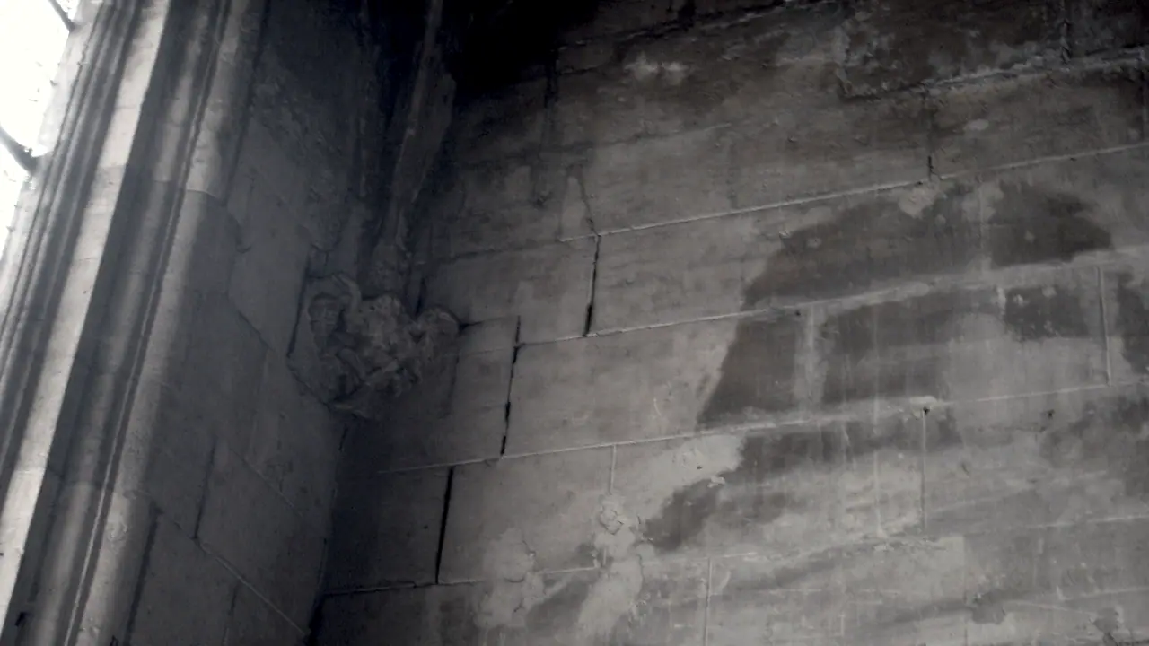 Mur de pierres de taille traversé par une fissure, sous une voûte, avec un motif sculpté et des traces d'humidité.