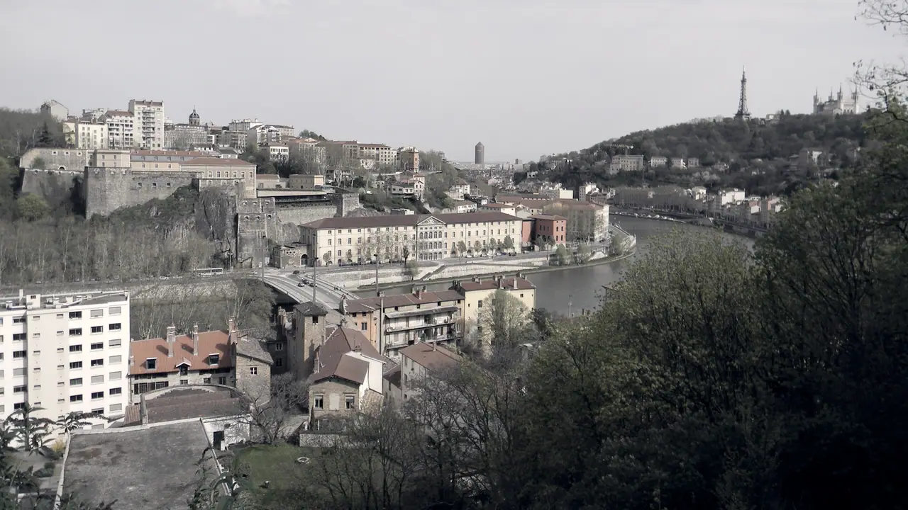 Panorama sur une ville traversée par une rivière, avec un fort en pierre sur l'éperon et une tour au sommet de la colline.