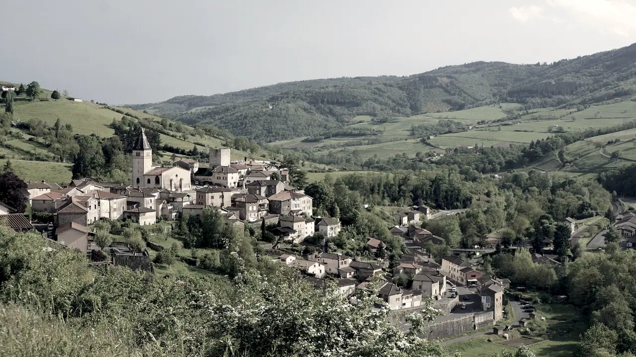 Village perché serré autour de son clocher, sur un versant boisé, avec des prés et des collines qui s'étendent au fond.