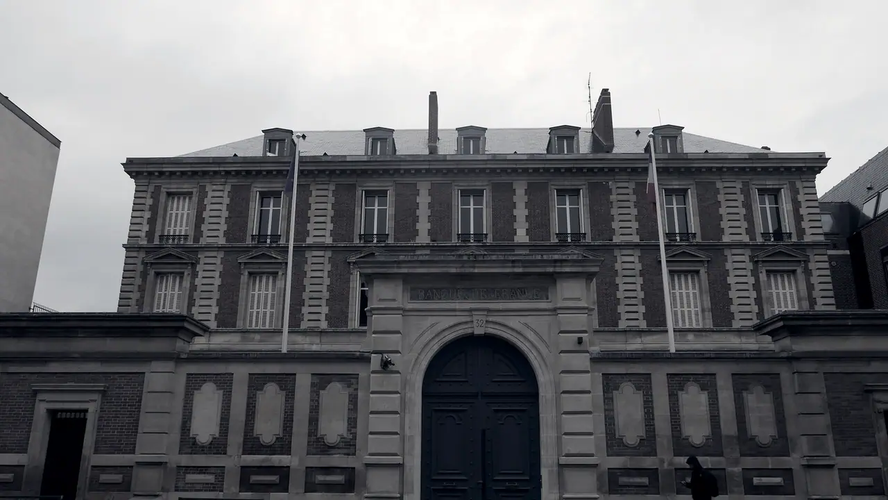 Façade institutionnelle en pierre et brique, avec son portail cintré, ses mâts de drapeau vides et ses fenêtres alignées sur trois niveaux.