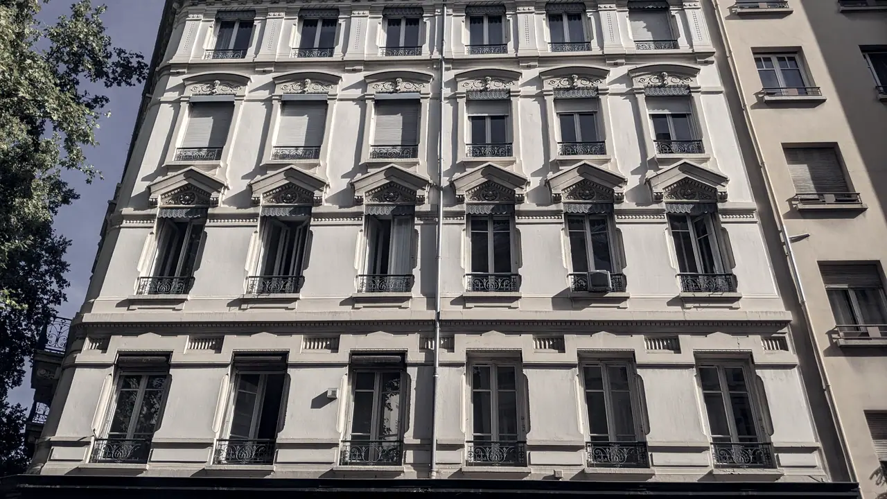 Immeuble de rapport lyonnais vu en contre-plongée : des étages de fenêtres et de balcons identiques, superposés jusqu'au toit.