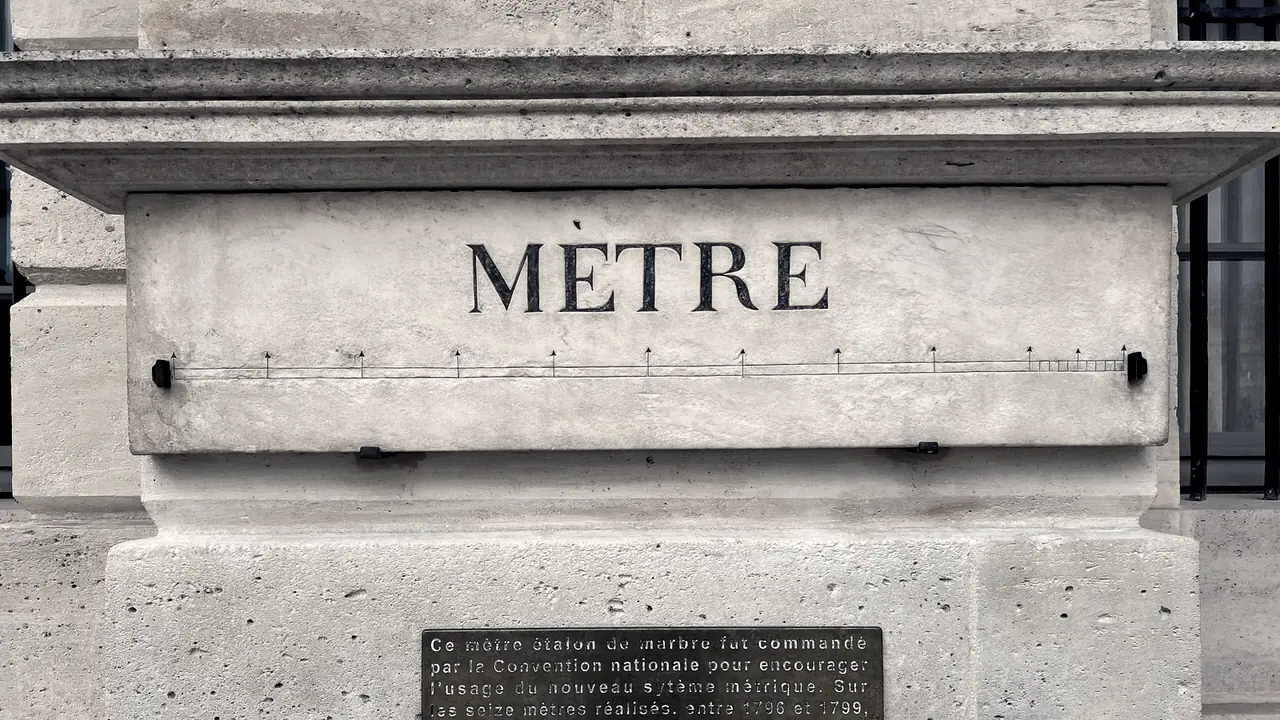 Mètre étalon de marbre scellé dans un soubassement de pierre : le mot MÈTRE gravé au-dessus de la règle, une plaque de bronze explicative en dessous.
