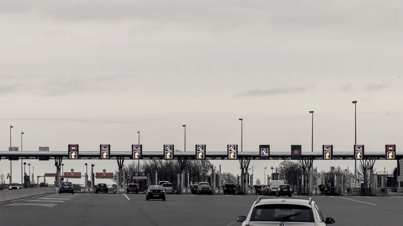 Barrière de péage autoroutier vue de face : une longue rangée de voies séparées par des îlots, sous un auvent continu.