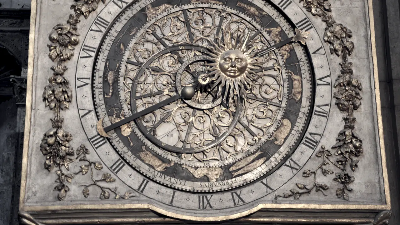 Cadran d'horloge astronomique en pierre, avec des chiffres romains sur le pourtour et un soleil sculpté au centre du mécanisme.