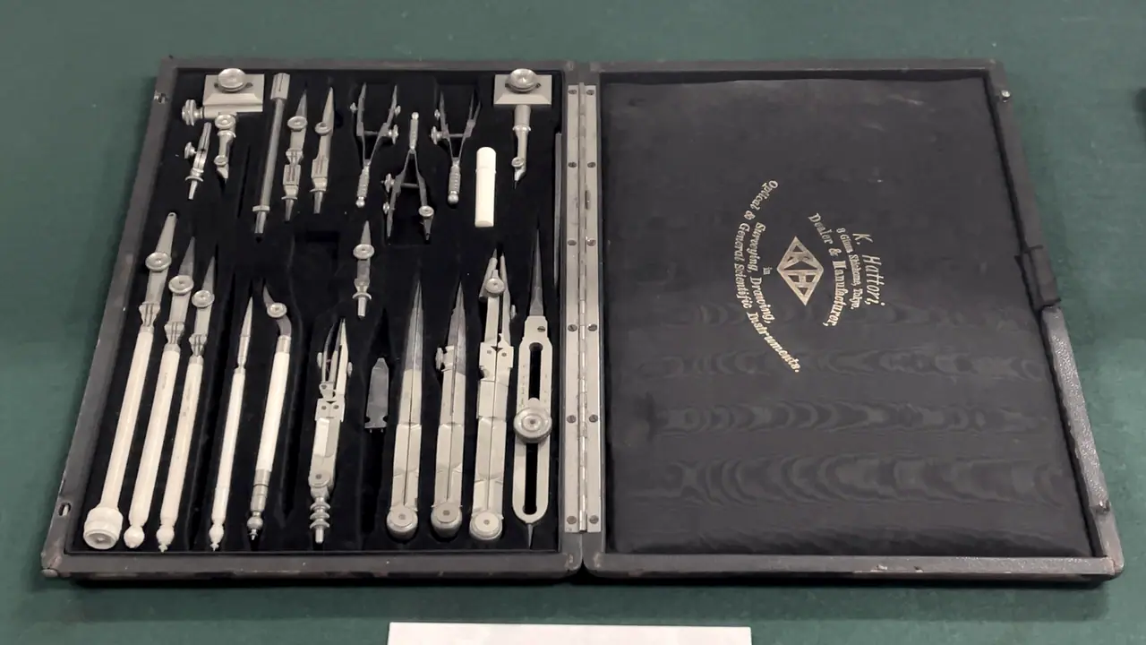 Étui ouvert d'instruments de dessin anciens : compas, tire-lignes et pointes rangés chacun dans son logement de velours noir, sur un tapis de feutre.