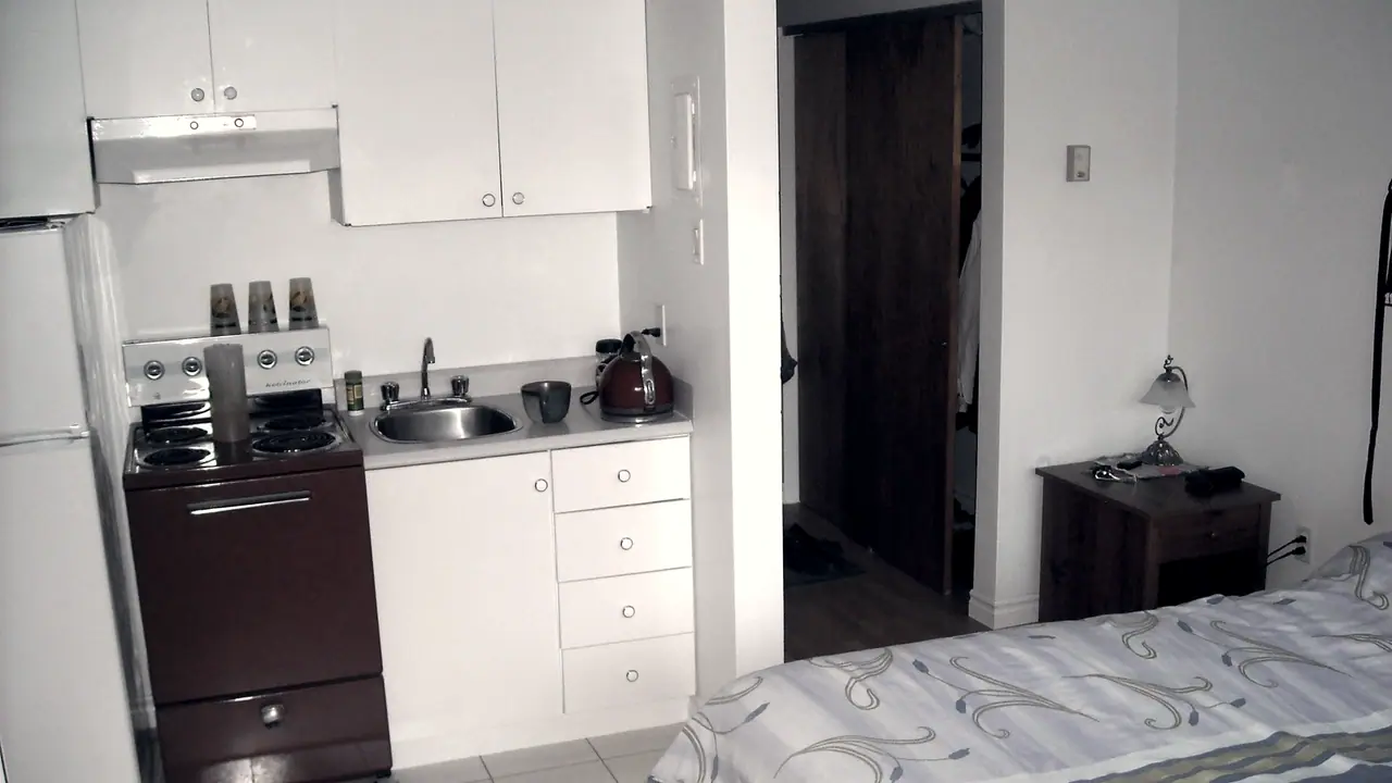 Coin cuisine d'un studio meublé, avec sa cuisinière, son évier, ses placards et le lit qui commence juste à côté.
