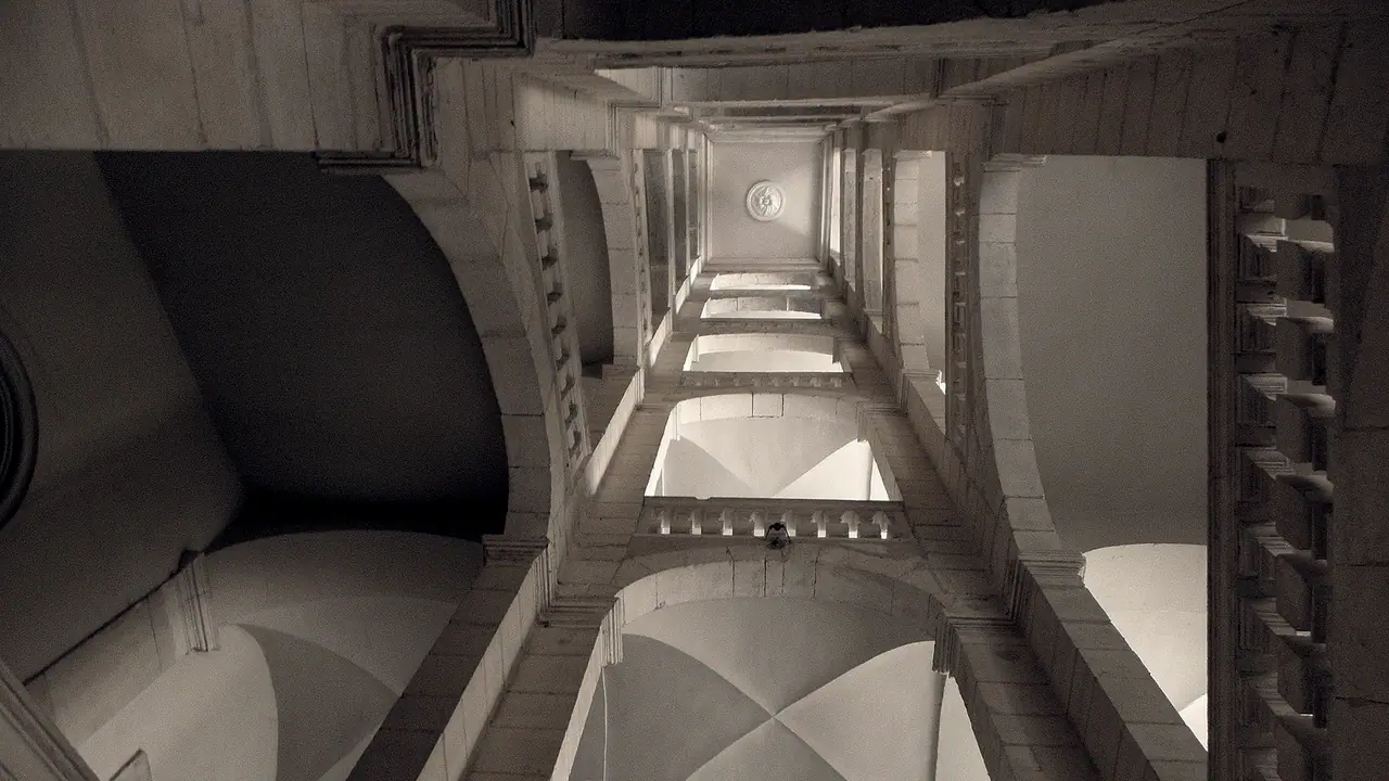 Cage d'escalier monumentale photographiée depuis le pied des marches, avec ses voûtes de pierre, ses balustrades et ses paliers qui se répètent.