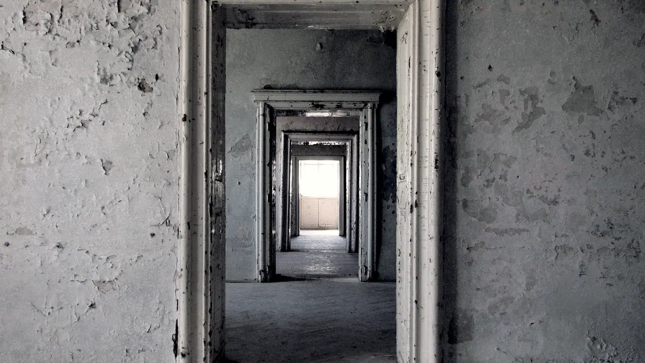 Enfilade de portes ouvertes dans un ancien couvent aux murs écaillés : les encadrements se succèdent jusqu'à une fenêtre éclairée au fond.