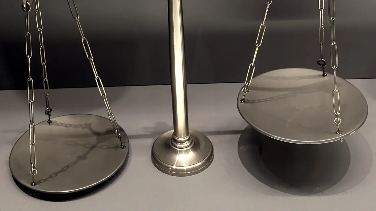 Balance à deux plateaux de laiton suspendus par des chaînettes de part et d'autre d'un fléau, sur un fond clair.