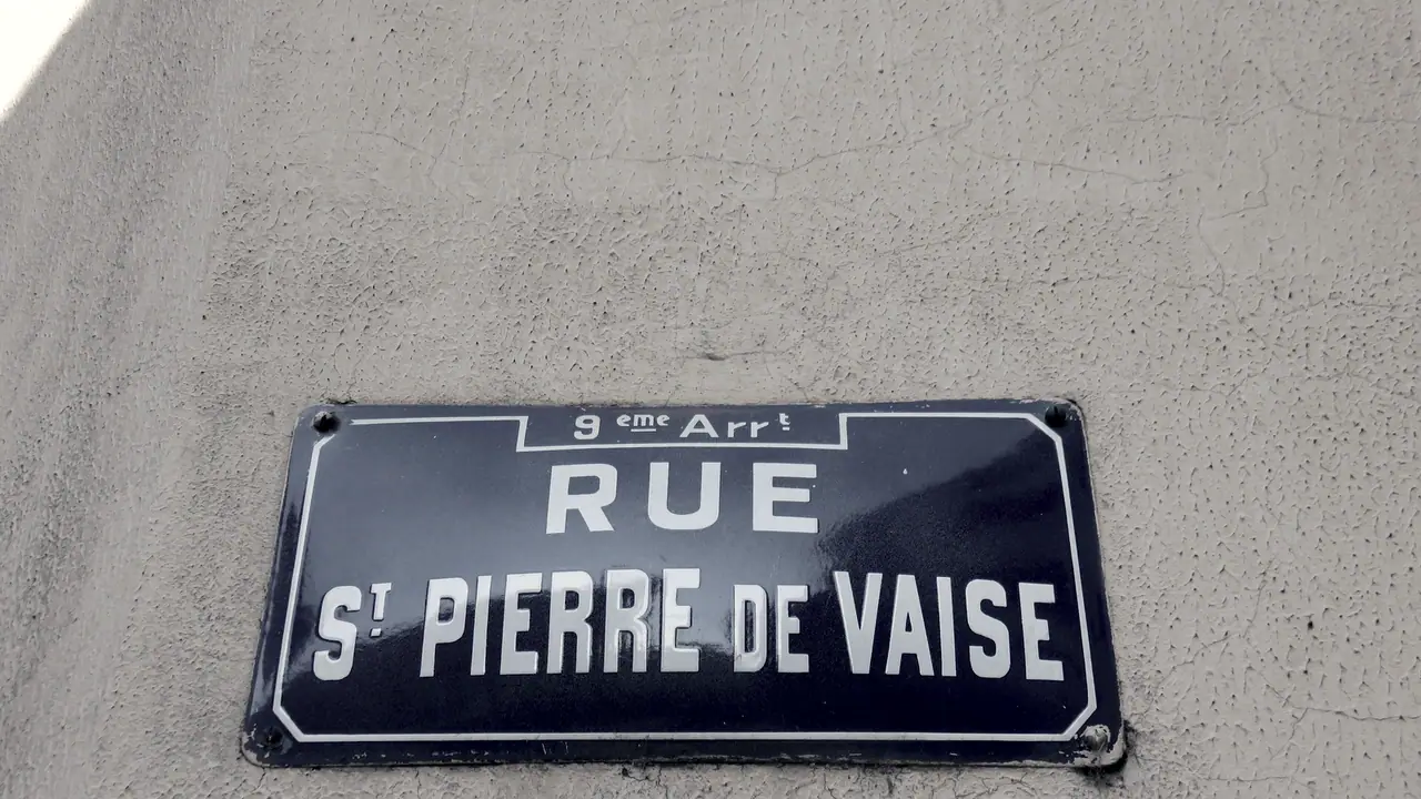 Plaque de rue émaillée vissée sur un mur en crépi rugueux, avec le numéro d'arrondissement inscrit au-dessus