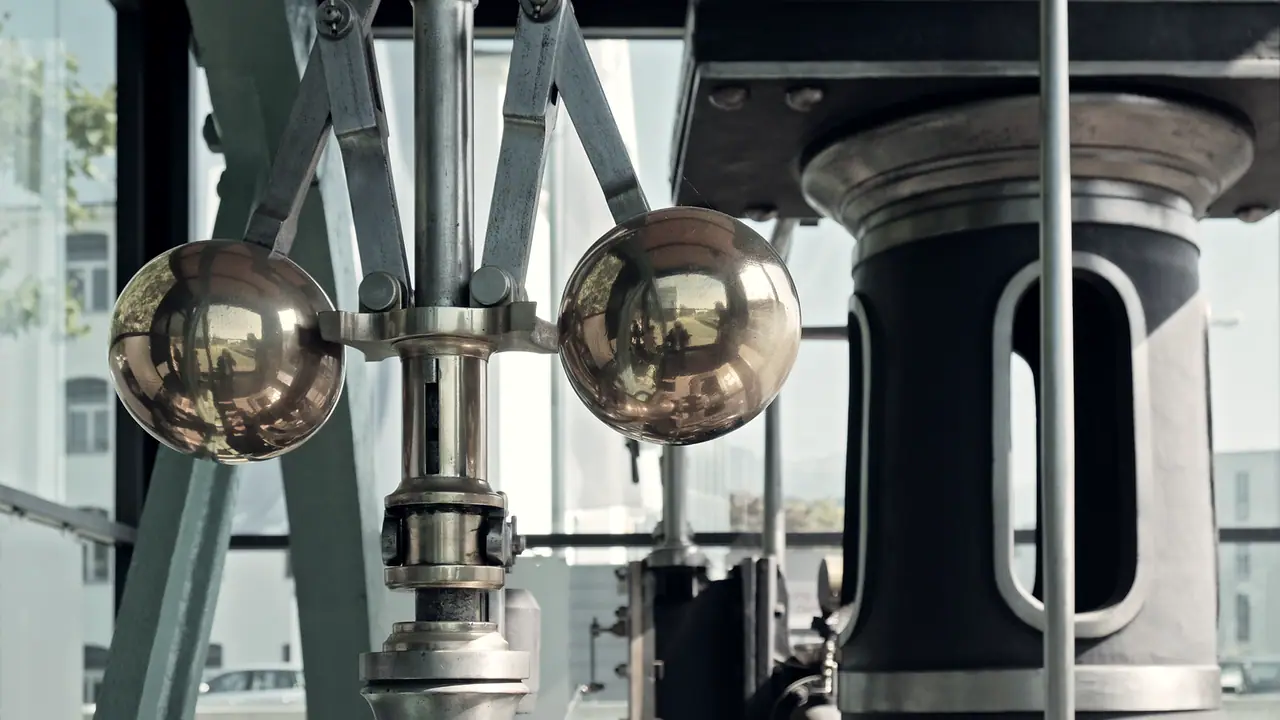 Régulateur à boules d'une machine à vapeur : deux sphères de laiton montées sur des bras articulés qui s'écartent avec la vitesse.