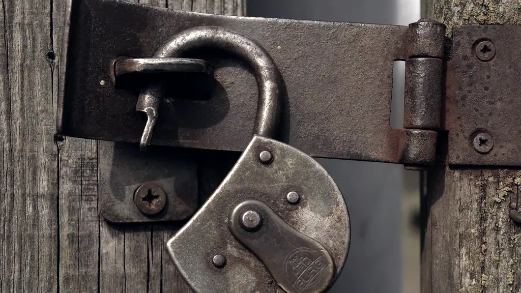 Cadenas de fer rouillé resté ouvert, son anse dégagée du moraillon, sur une porte de bois usée par la pluie.