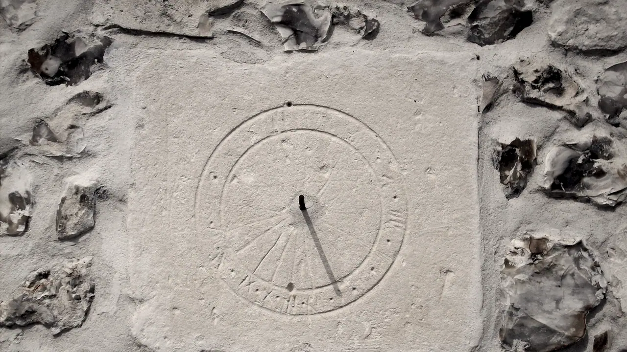 Cadran solaire gravé dans un mur de calcaire ; la tige projette son ombre sur les heures, entre des moellons irréguliers.