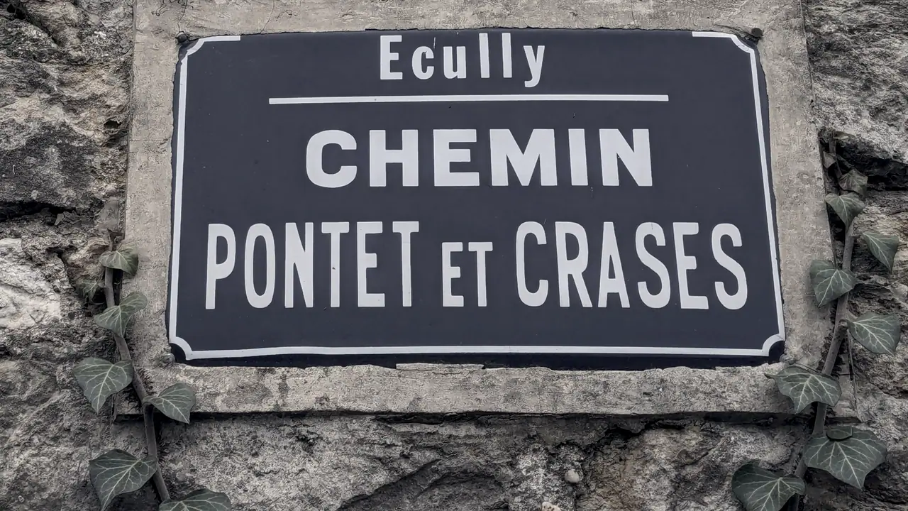 Plaque de rue émaillée vissée sur un mur de pierre : elle porte le nom de la commune d'Écully au-dessus de celui du chemin.