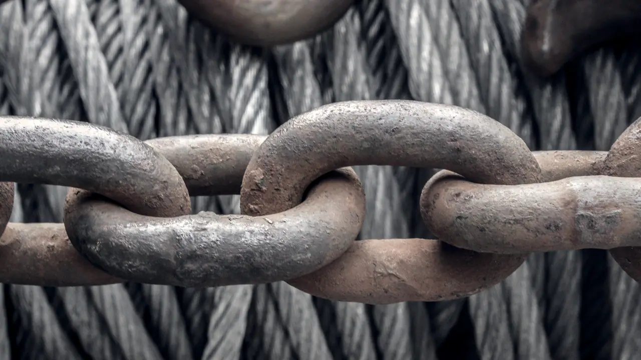 Gros maillons de chaîne rouillés passés les uns dans les autres, devant les torons d'un câble d'acier enroulé.